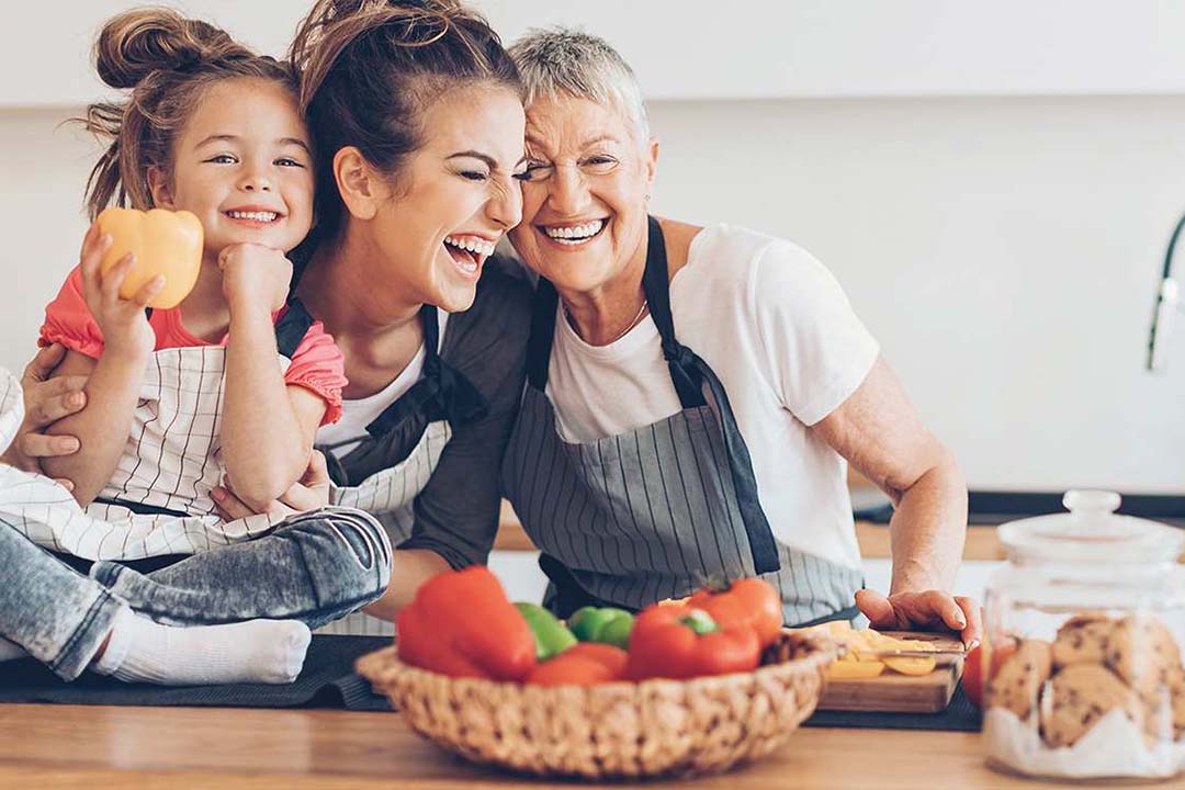 Zwei Frauen mit Kind stehen lachend in der Küche